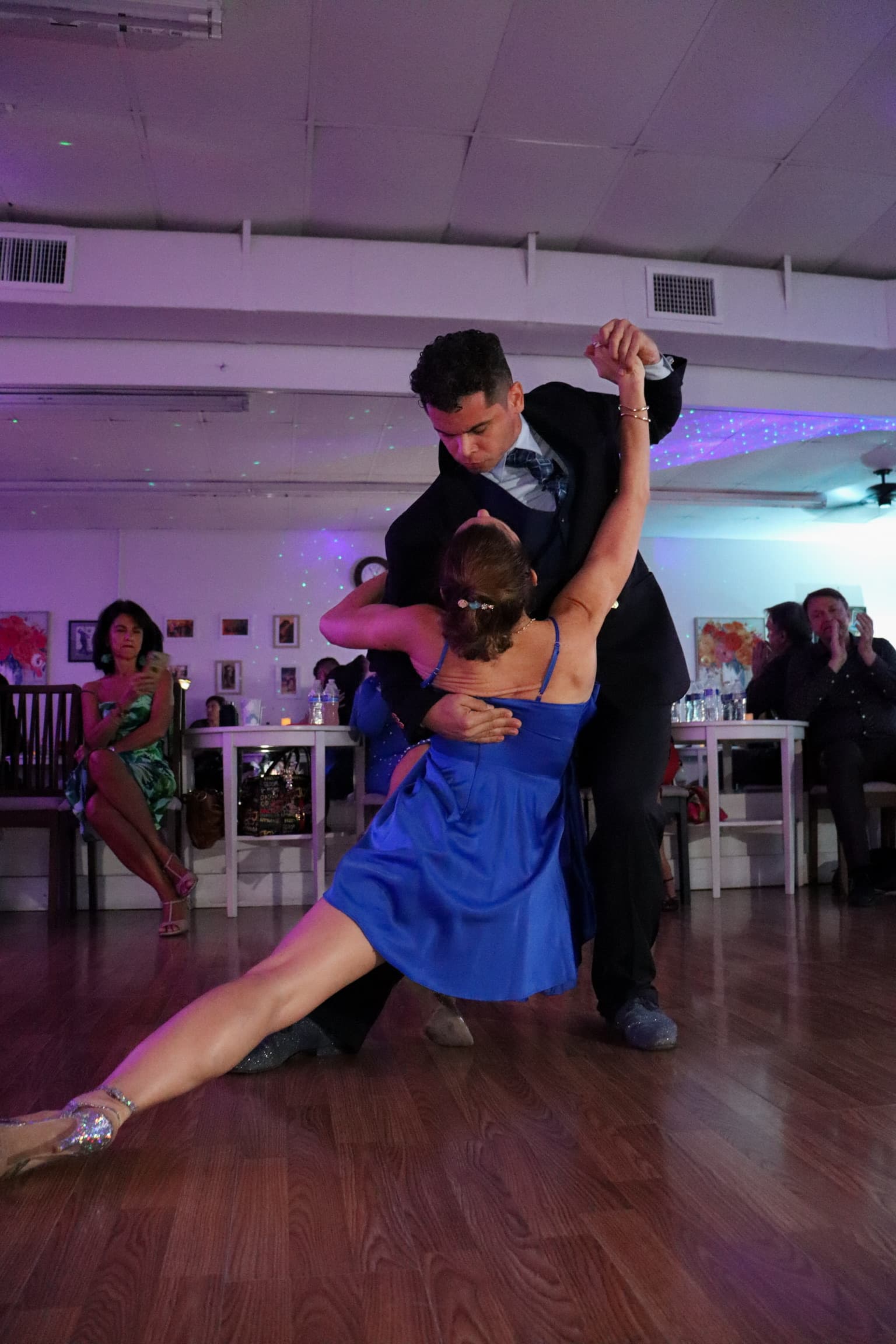 Man in a suit dips a woman in a blue dress on a wooden dance floor.
