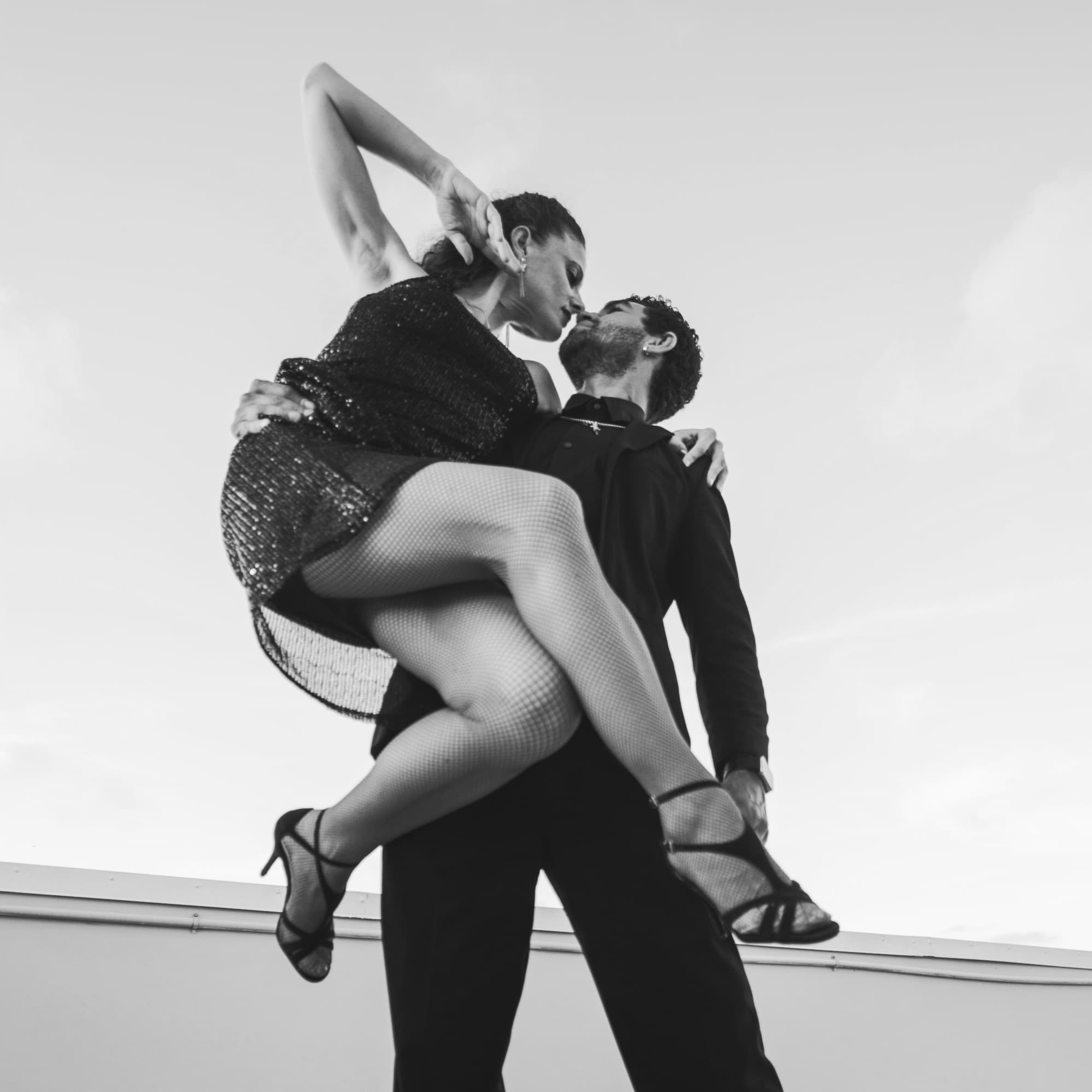 Man lifts a woman in a sequined dress during an intimate, dramatic dance pose.