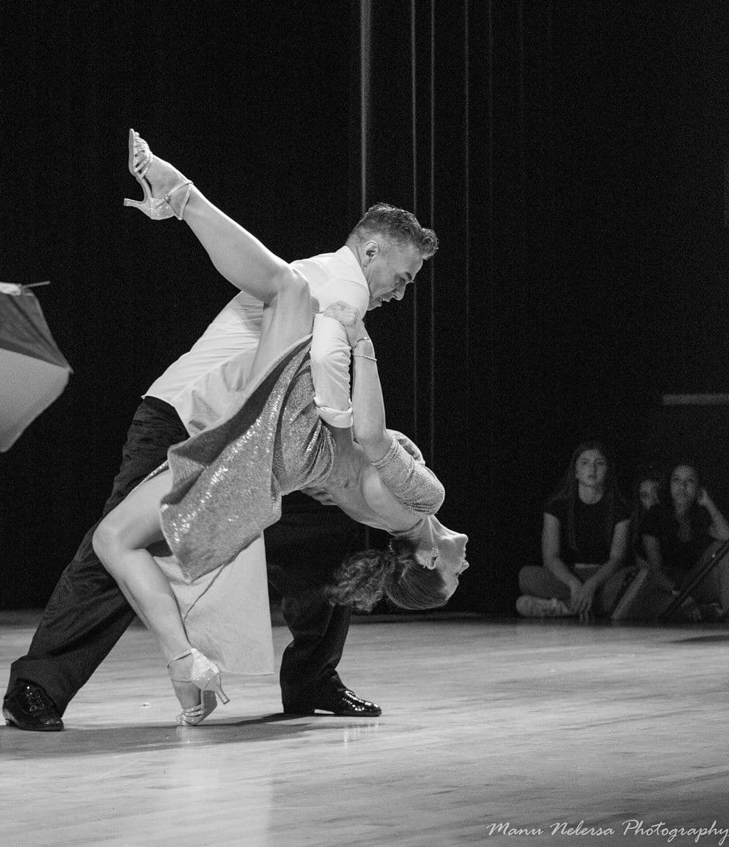 Man dips woman in sparkly dress with leg extended during a dramatic ballroom dance.