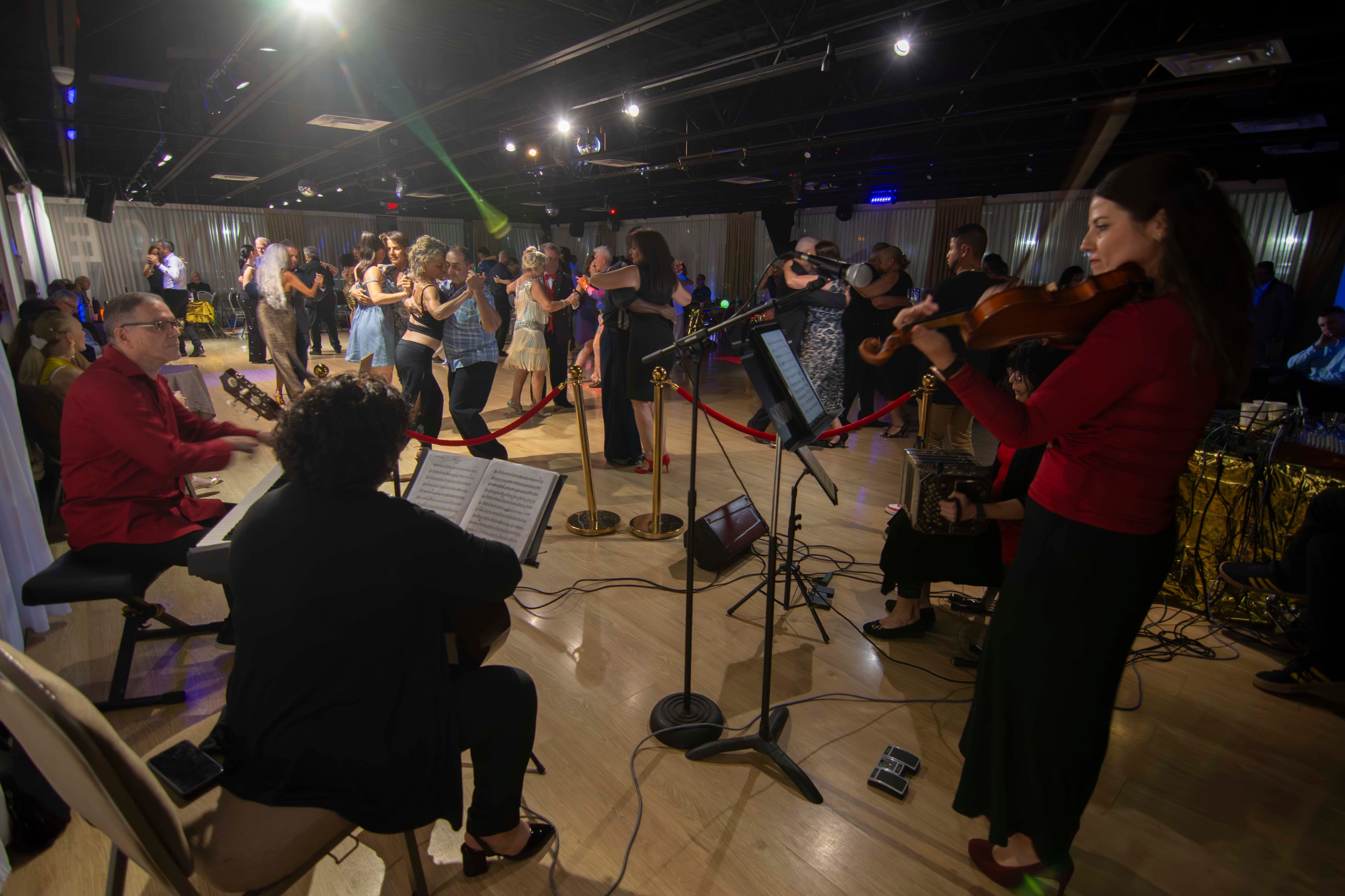 Live band performs in the foreground as couples dance in a dimly lit ballroom.