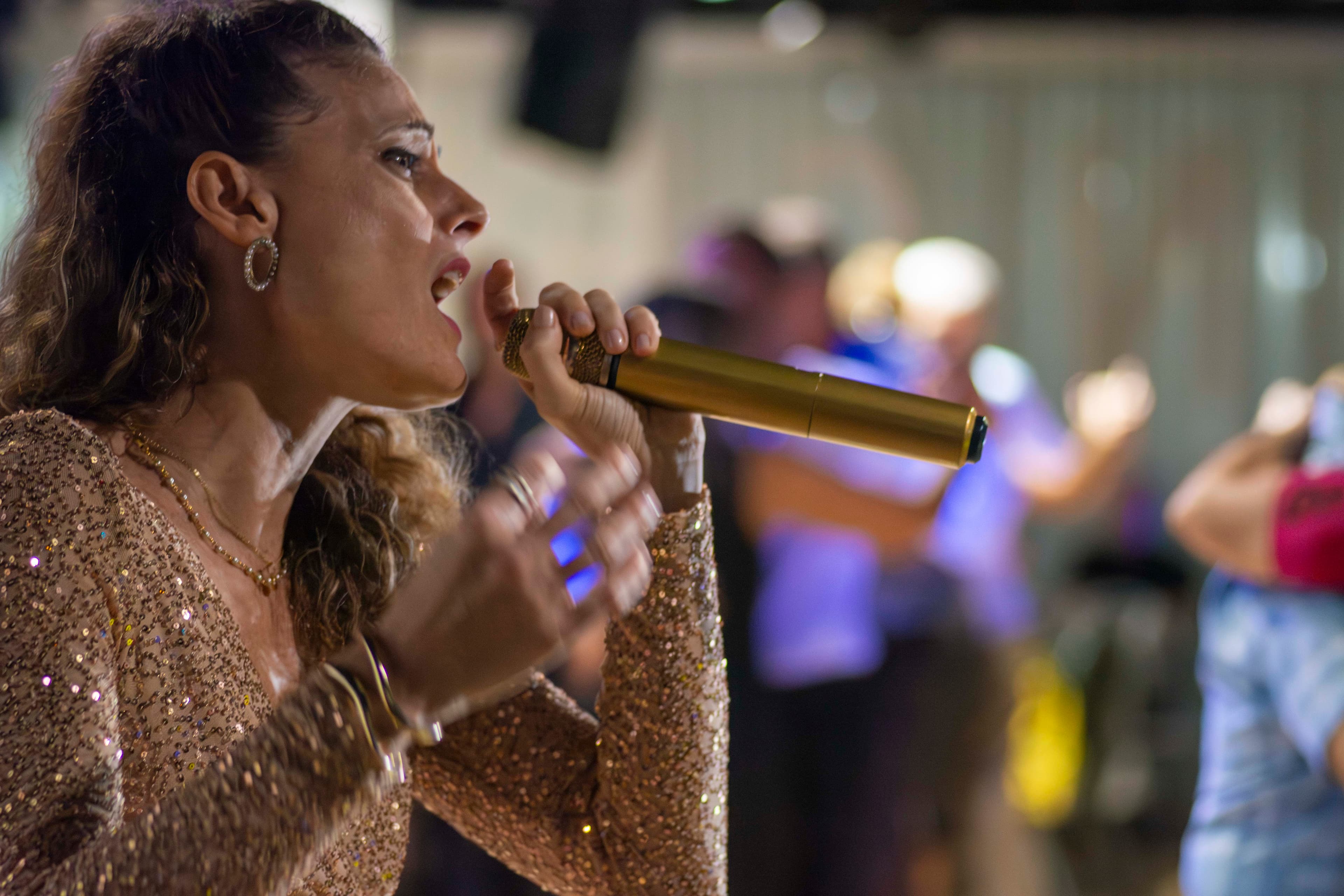 Woman in a shimmering gold sequined dress sings passionately into a gold microphone.