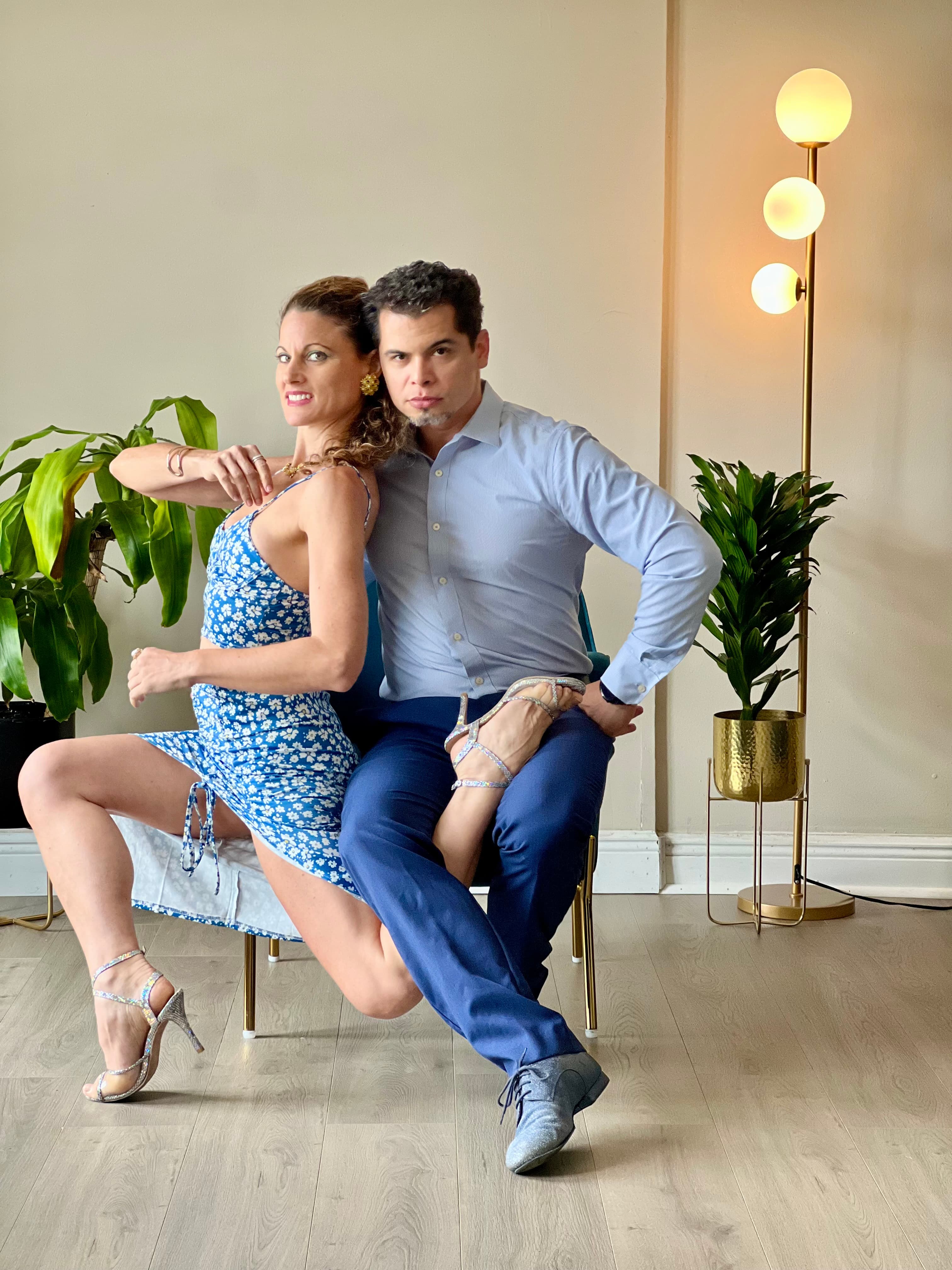 Man and woman in blue outfits pose elegantly in a room with green plants.