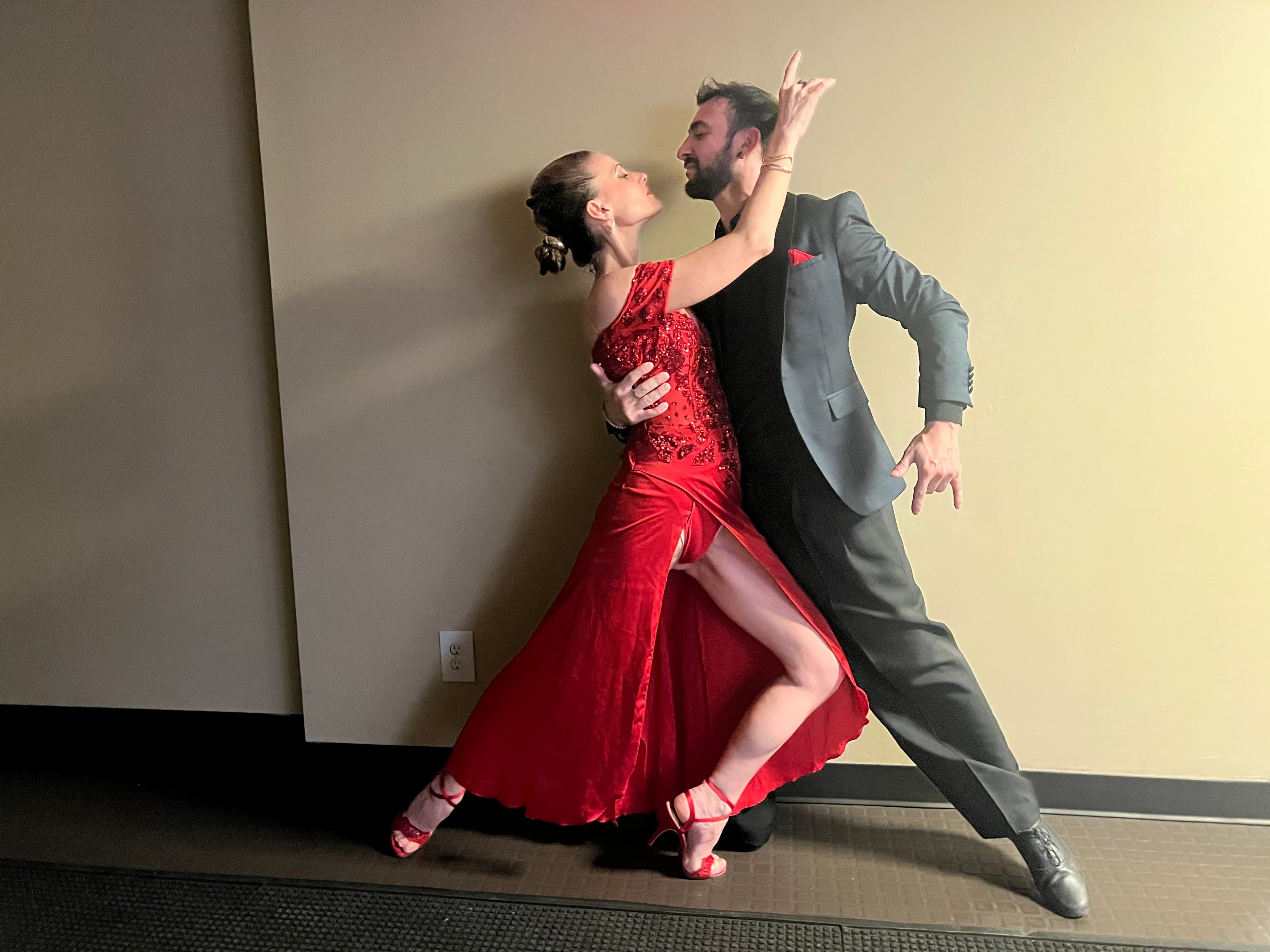 Man in a suit and woman in a red sequined dress strike a tango pose.