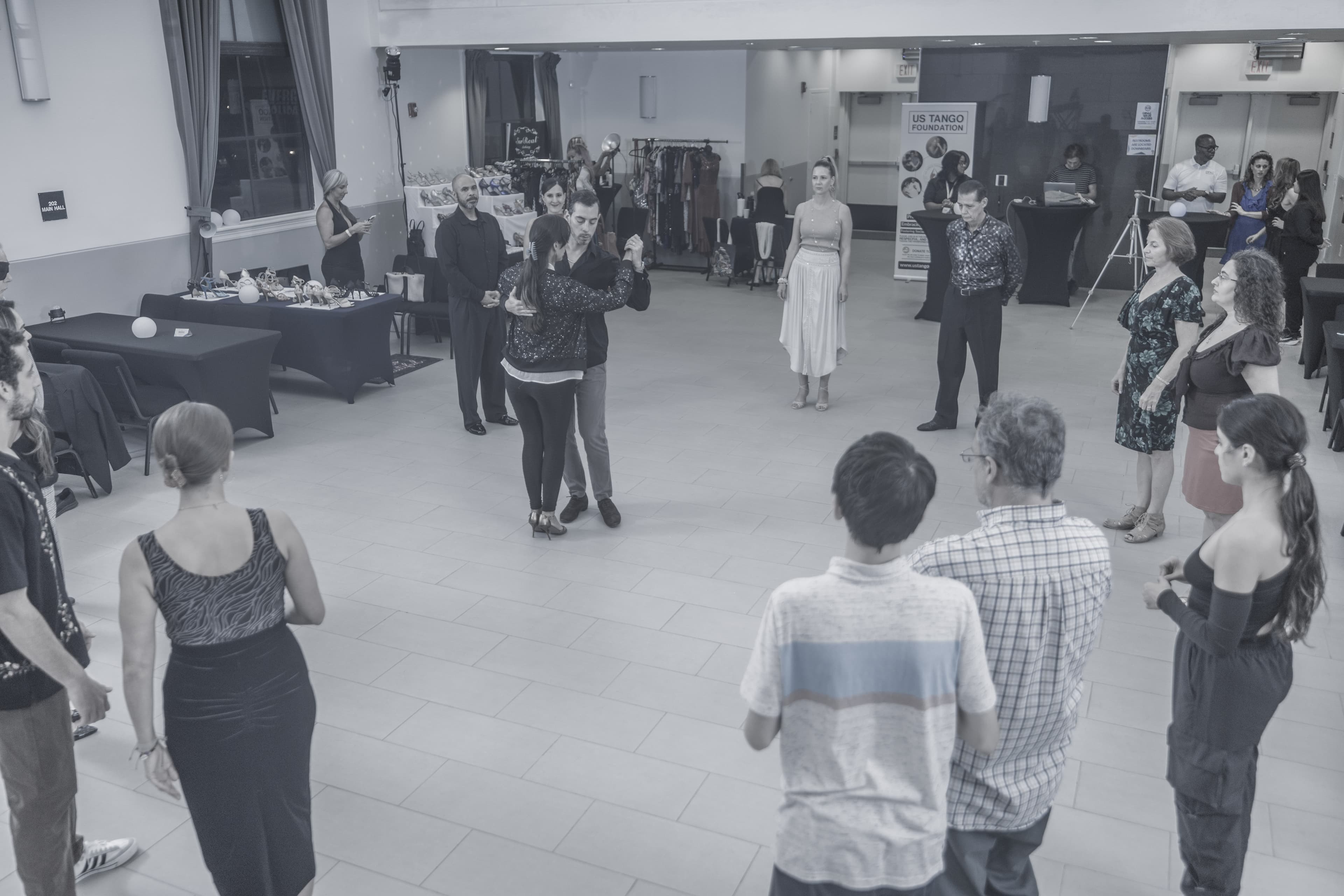 A couple performs a tango dance in a large hall while a group watches.